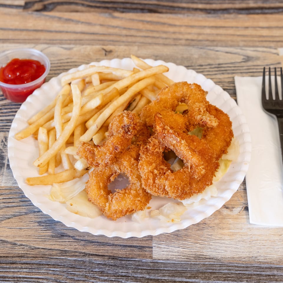 Crispy breaded shrimp and French fries served on a paper plate with ketchup and cutlery on a wooden table.