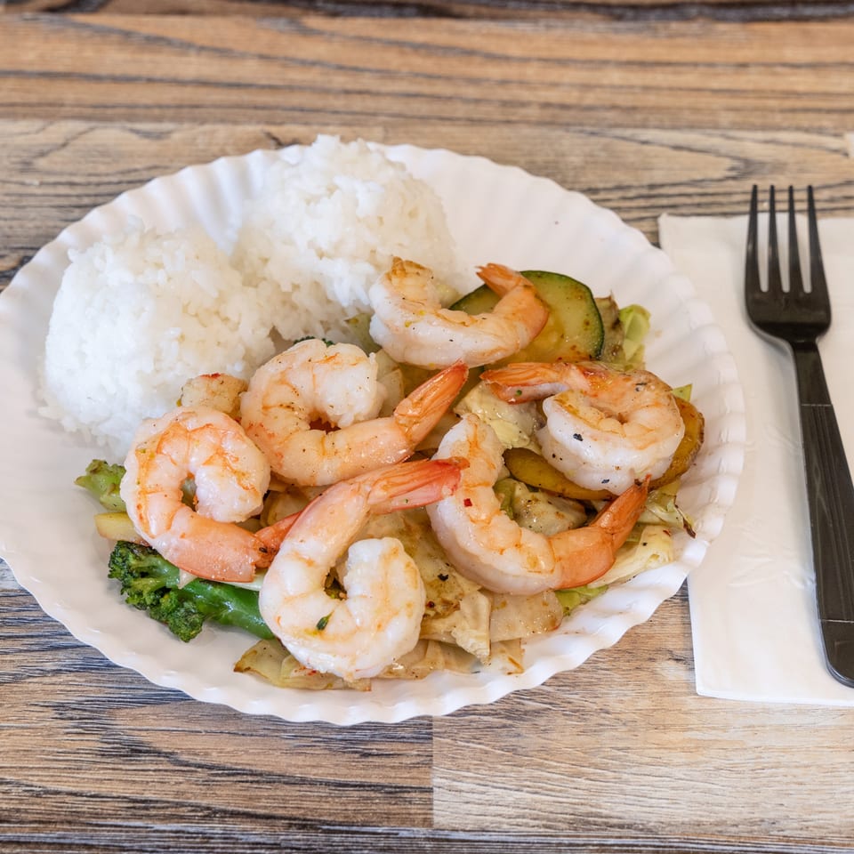 Plate of sautéed shrimp, white rice, and mixed vegetables with fork and knife on a wooden table.