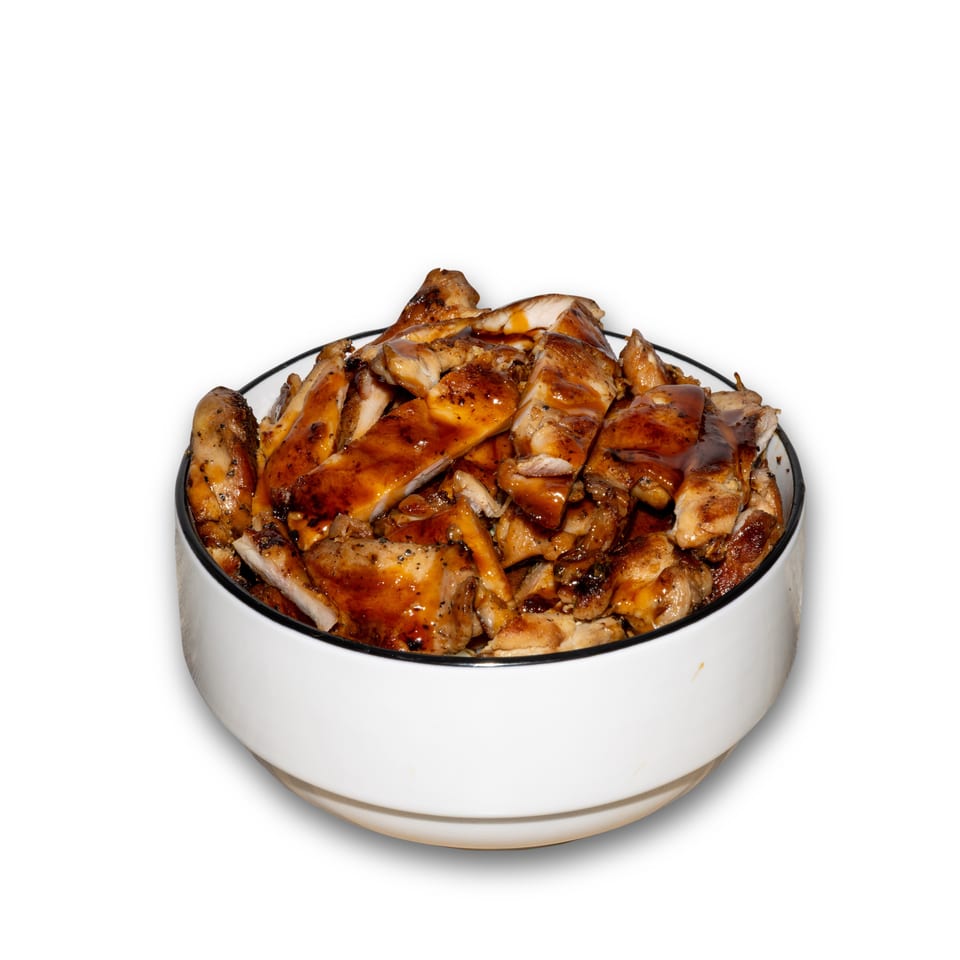 Bowl overflowing with glossy grilled chicken pieces against a plain white background.