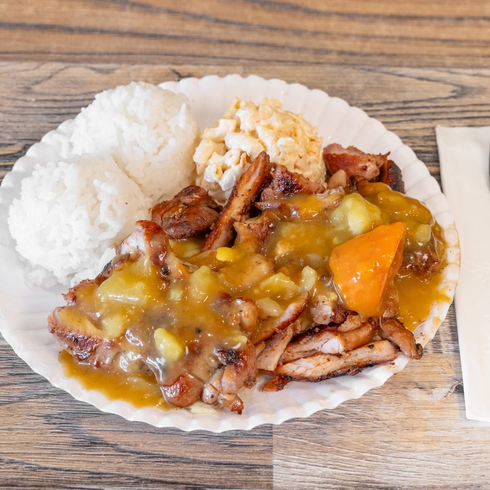 Plate of white rice, grilled meat, vegetables, and macaroni salad with gravy on a wooden table.