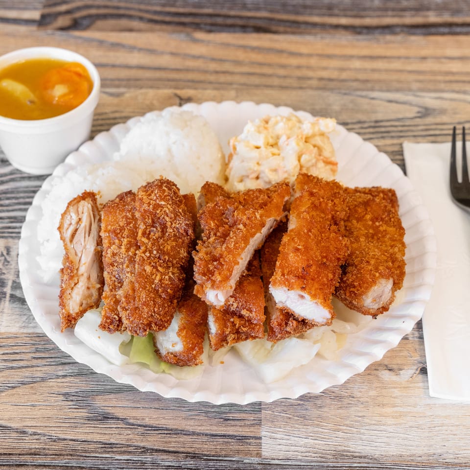 Plate of crispy breaded chicken pieces with white rice, salad, and orange dipping sauce on a wooden table.