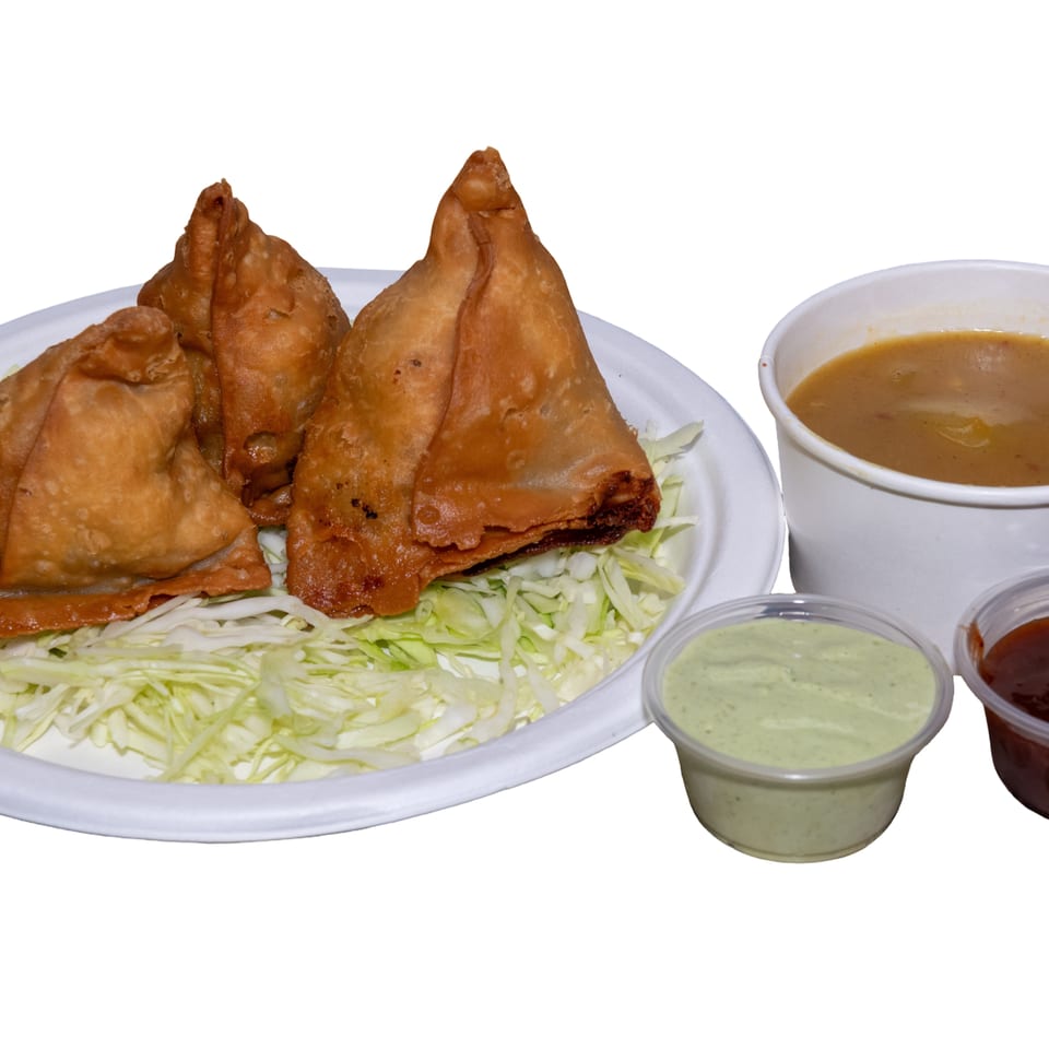 Crispy fried samosas served over shredded lettuce with bowls of curry, green chutney, and red dipping sauce.