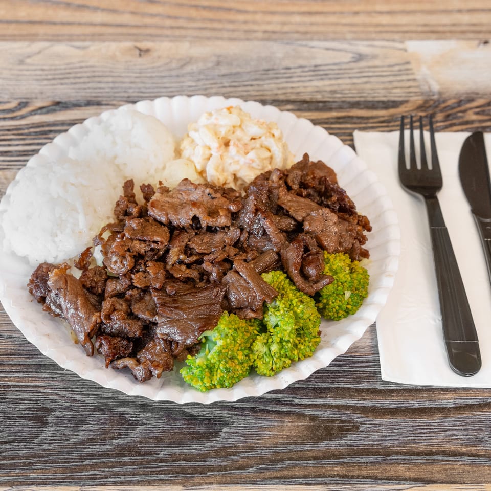 Plate of sliced grilled beef with white rice, creamy salad, and steamed broccoli on a wooden table.