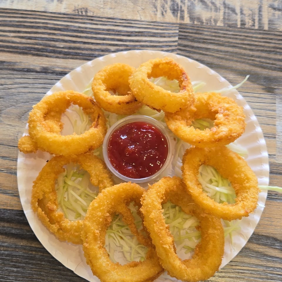 Crispy golden fried onion rings arranged over shredded lettuce with a cup of red dipping sauce on a white plate.