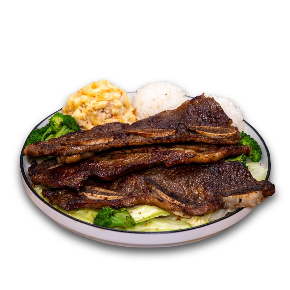 Plate of grilled beef ribs served with white rice, macaroni and cheese, broccoli, and cabbage.