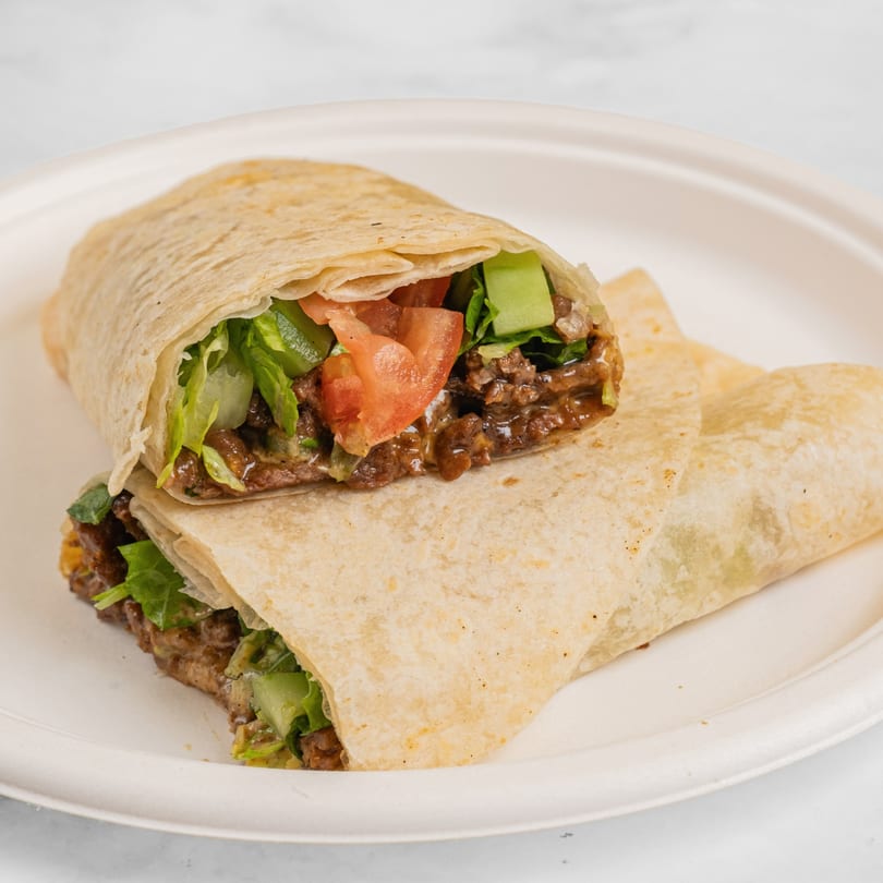 Two Hawaiian wraps, one cut open to show beef, lettuce, tomatoes, and cucumbers, on a white plate.