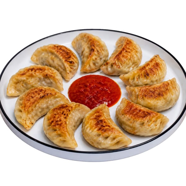 Golden pan-fried dumplings with crispy edges encircling a red chili dipping sauce on a white plate.