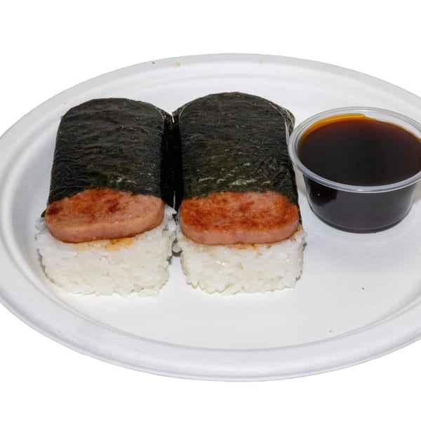 Two Spam musubi, rice topped with grilled Spam and wrapped in nori, with a side of soy sauce.