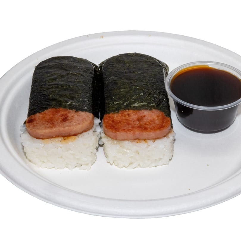 Two Spam musubi, rice topped with grilled Spam and wrapped in nori, with a side of soy sauce.