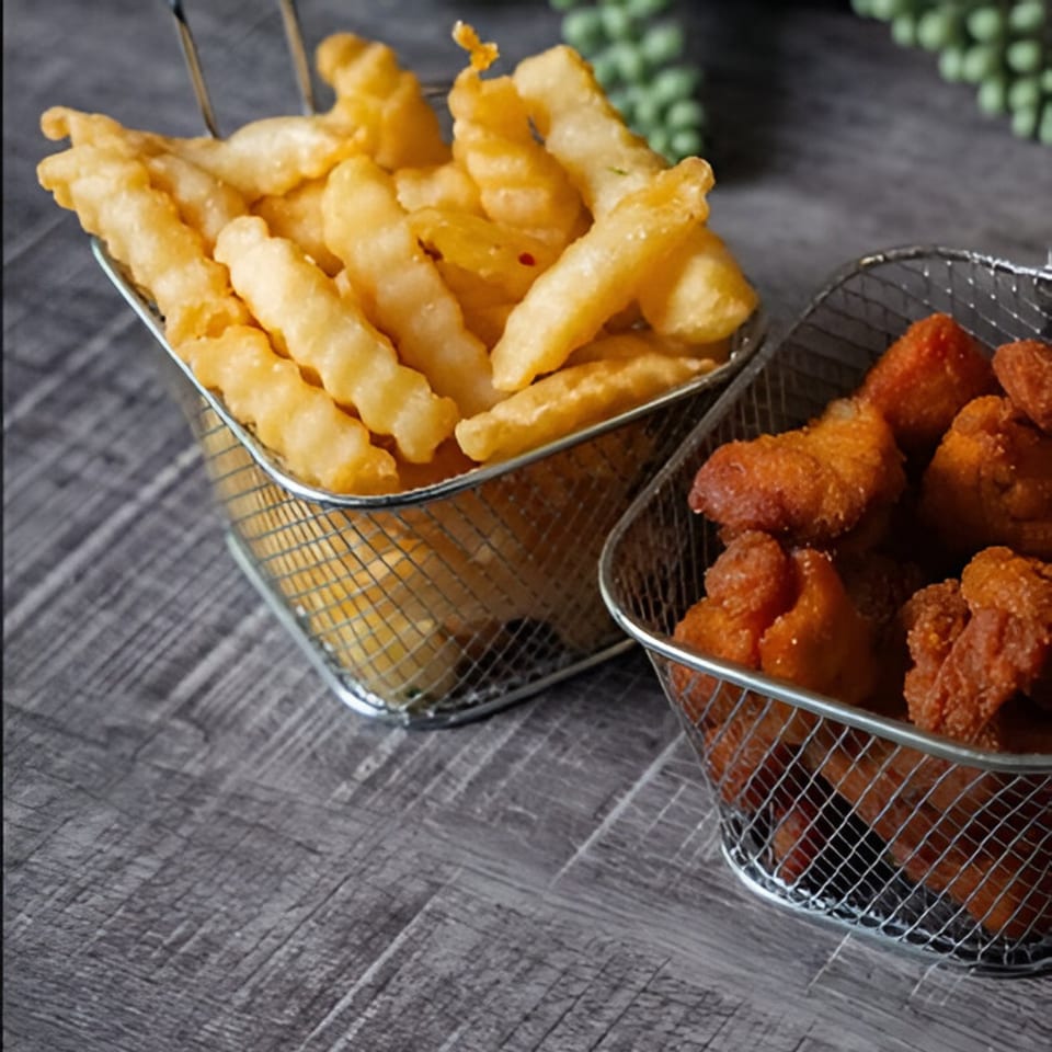 Crispy golden french fries and chicken nuggets in metal baskets on a dark wooden surface.